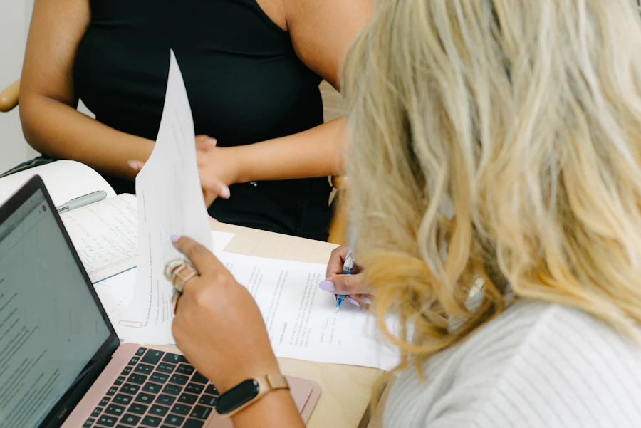 Two people reviewing printed material beside a laptop